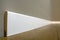 Wooden or plastic white floor plinth installation in big empty room on wooden floor and white plastered stucco walls background.