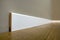 Wooden or plastic white floor plinth installation in big empty room on wooden floor and white plastered stucco walls background.