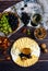 Wooden plate with different types of cheese, a basket with dark and green grapes, walnut, dates and a glass of white wine on a