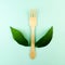 Wooden plywood fork with green leaves wings on turquoise green mint background. Creative zero waste concept