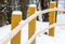 Wooden pole handrail bent beige fence winter road in the forest. yellow bars snow cap