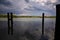 Wooden poles of a mooring in the water with their reflections casted in the water of a river in the italian countryside