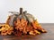 Wooden pumpkin surrounded by artificial orange leaves sitting on a wooden cutting board with a white wall behind.  Simple