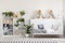 Wooden rack with books, fresh plants and cushions in white bedro