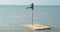 Wooden raft with black pirate flag on pole floats on sea