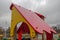 Wooden red sloping roof with yellow gable on the playground, covered with raindrops on the background of a gloomy gray sky