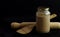 Wooden rolling pin with spoon and sourdough starter in a glass jar isolated on black background