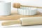 Wooden rolling pin, white measuring cup, baking form and honey dipper on cutting board. White tabletop background.