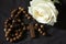 Wooden rosary with Jesus Christ holy cross crucifix and white rose on black background. Catholic rosary symbil