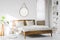 A wooden rustic bed frame and a home library bookcase in a natural, sunlit hotel room interior with white walls