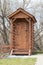 Wooden rustic toilet on early spring trees background. Modern rural wooden toilet. Wooden ecological composting toilet on
