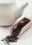 Wooden scoop of black loose tea with white ceramic teapot on white