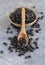 Wooden scoop full of dry black beans on grey table closeup