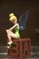 A wooden sculpture of a Disney character of Tinker Bell fairy sitting on the wooden letter block