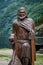 Wooden sculpture of norse viking sailor with forest and fjord background.