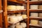 Wooden shelves in basement, cellar with round cheese. Home production