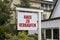 Wooden sign in front of a house with message For Rent, For Sale, and the german words for sale - zu verkaufen