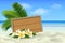 Wooden signboard on tropical beach with white sand, plumeria flowers and palm leaves. Summer background with place for text