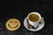 Wooden smile on a dark black texture background. On the edge you can find a cup of coffee with espresso, on the saucer