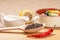 Wooden spoon with black peppercorn, dried red pepper on cutting board and ceramic soup bowl with saltwort, sauceboat and cut lemon