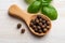 Wooden spoon full of allspice jamaica pepper near green basil leaves on a white wooden table. Whole dried pimento berries close-up