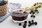 Wooden spoon on a glass bowl with blackberry jam and several blackberries on a white background