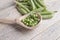 A wooden spoon with green peas on the background of pods lies on a light table. The concept of vegan products