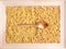 A wooden spoon rests on raw farfalle and fusilli pasta. Wooden frame