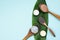 Wooden spoons with black, red, orange and gray clay on a green palm leaf on a pastel blue background. Cream, balm and powder to