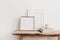 Wooden square and white portrait frame mockups on vintage bench, table. Cup of coffee on pile of books. White wall