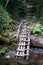 A wooden staircase in the mountains descends to the mountain river from the waterfall