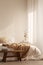 Wooden stool in front of bed with blanket in natural white bedroom interior with plant