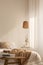 Wooden stool in front of bed with linen blanket in natural bedroom interior with lamp