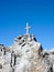 wooden summit cross on a sharp and jagged mountain peak under a blue sky