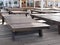 Wooden sun beds stand in the shade on a platform without a single vacationer next to the sea in the early summer morning.