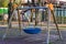 A wooden swing with a circular blue rubber seat in a public park Italy, Europe