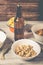 On a wooden table a bottle of beer, dried fish, chips, crackers and nuts
