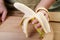 On a wooden table on a cutting board, a woman holds a banana peeled from her skin in her hand.