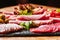 Wooden table filled with delicious cold meat selection. A plate with a variety of sausages with green vegetables green lettuce,