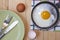 Wooden table with fried egg, eggshells, knife and fork, dish towel