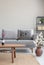 Wooden table in front of grey settee in simple apartment interior with flowers and carpet