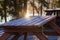 Wooden table in the garden of a closed restaurant. There is a dust of snow on the table. The sun shines through the trees