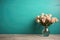 Wooden table with glass vase with bouquet of roses flowers near empty, blank turquoise wall. Home interior background