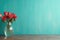 Wooden table with glass vase with bouquet of roses flowers near empty, blank turquoise wall. Home interior background