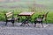 Wooden table and public benches with black metal baroque style support frame mounted on gravel plateau with view uncut grass and