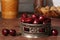 On a wooden table there is a metal openwork vase full of ripe juicy red cherries