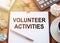 On a wooden table there is an office sheet of paper with the text Volunteer activities. Business workspace with calculator,