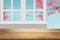 Wooden table top with white window frame and blurlly Sakura flowers branch against blue sky