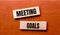 On a wooden table are two wooden blocks with the text question MEETING GOALS