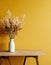 Wooden table with vase with bouquet of dried field flowers near empty, blank mustard wall